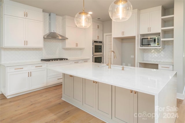 kitchen with a center island with sink, wall chimney range hood, sink, decorative light fixtures, and stainless steel appliances