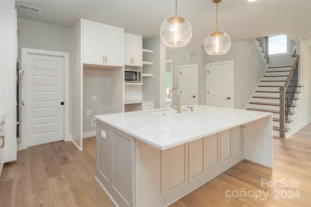 kitchen with white cabinets, sink, an island with sink, decorative light fixtures, and light hardwood / wood-style floors