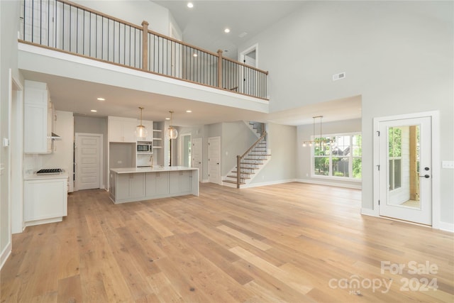 unfurnished living room featuring light hardwood / wood-style flooring, a towering ceiling, a chandelier, and sink