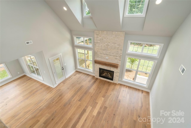 unfurnished living room featuring a fireplace, a healthy amount of sunlight, a high ceiling, and hardwood / wood-style flooring