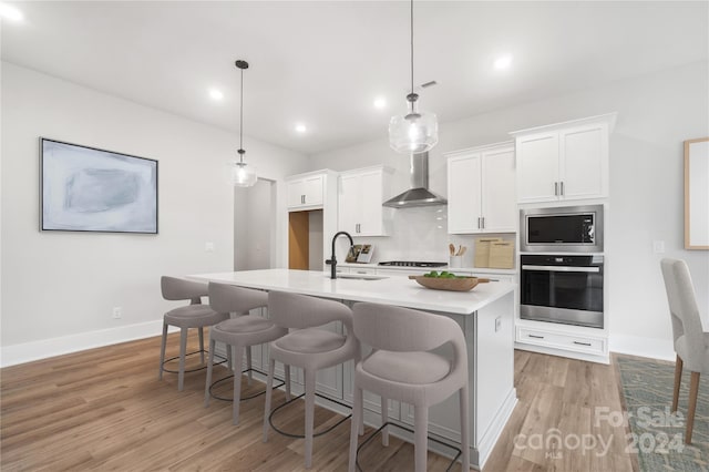 kitchen featuring hanging light fixtures, sink, stainless steel appliances, and wall chimney range hood