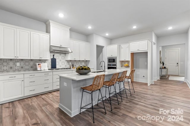 kitchen featuring appliances with stainless steel finishes, light wood-type flooring, white cabinetry, and an island with sink