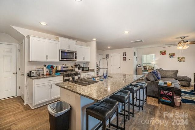 kitchen featuring dark hardwood / wood-style flooring, stainless steel appliances, white cabinetry, and a center island with sink