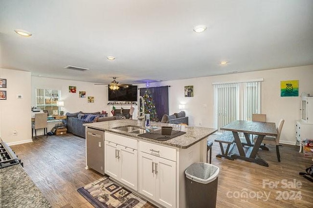 kitchen featuring a center island with sink, sink, stainless steel dishwasher, light stone counters, and white cabinetry