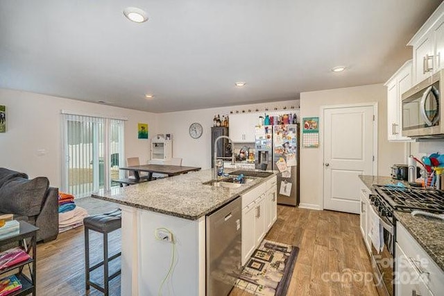 kitchen with dark stone counters, stainless steel appliances, a kitchen island with sink, light hardwood / wood-style flooring, and white cabinets