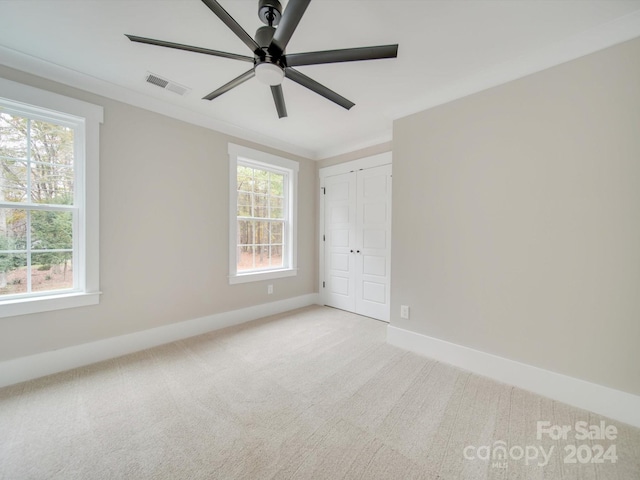 unfurnished bedroom featuring ceiling fan, a closet, light colored carpet, and multiple windows