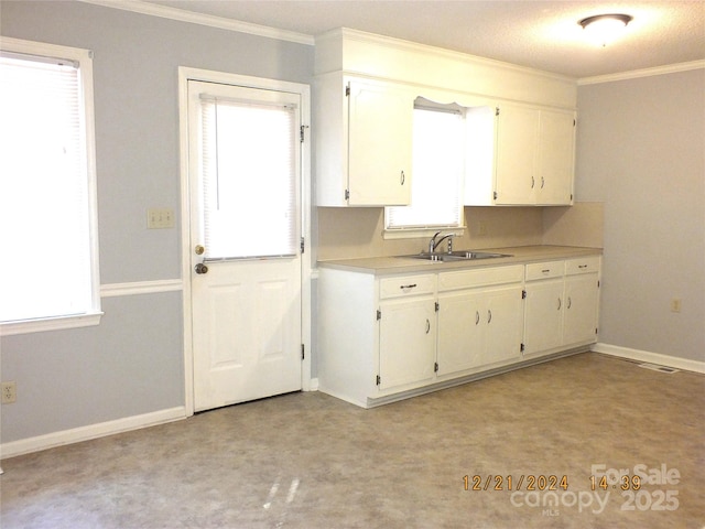 kitchen with baseboards, ornamental molding, light countertops, white cabinetry, and a sink