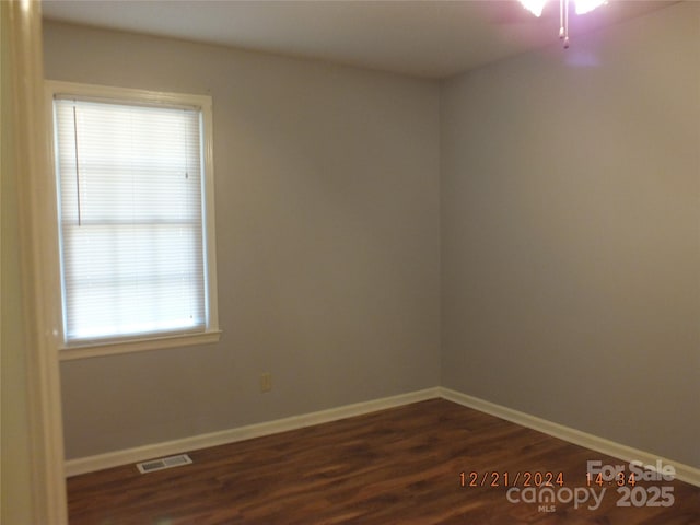 empty room featuring visible vents, dark wood finished floors, and baseboards