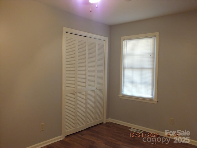 unfurnished bedroom with a closet, visible vents, dark wood finished floors, and baseboards