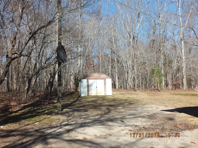 view of yard with an outdoor structure, a view of trees, and a storage unit