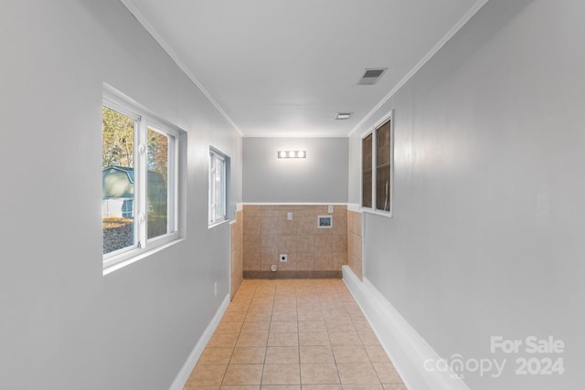 hall with light tile patterned floors, ornamental molding, a wealth of natural light, and tile walls