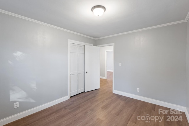 unfurnished bedroom featuring a closet, ornamental molding, and hardwood / wood-style flooring