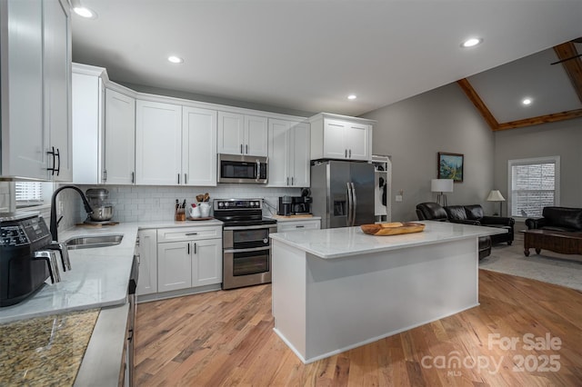 kitchen with appliances with stainless steel finishes, tasteful backsplash, vaulted ceiling, sink, and white cabinetry