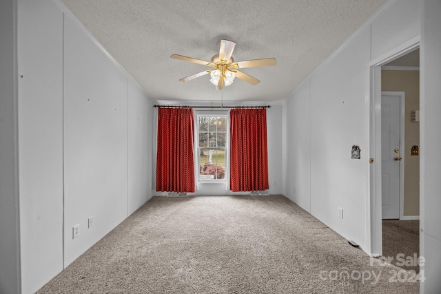 empty room with a textured ceiling, carpet floors, ceiling fan, and crown molding