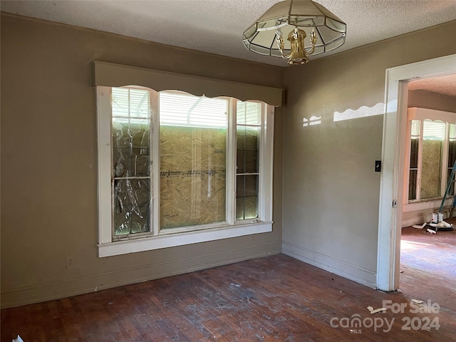 unfurnished room with a textured ceiling, dark hardwood / wood-style floors, and a notable chandelier