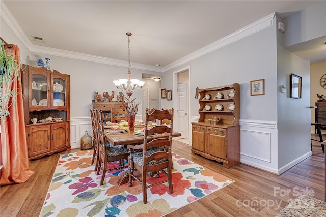 dining space featuring light wood-type flooring, an inviting chandelier, and ornamental molding