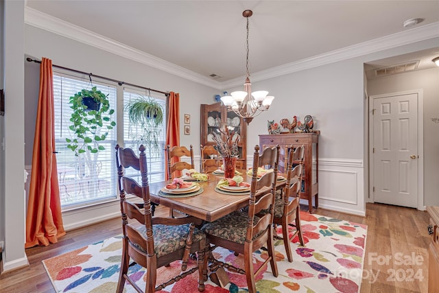 dining room with a healthy amount of sunlight, light hardwood / wood-style floors, ornamental molding, and a notable chandelier