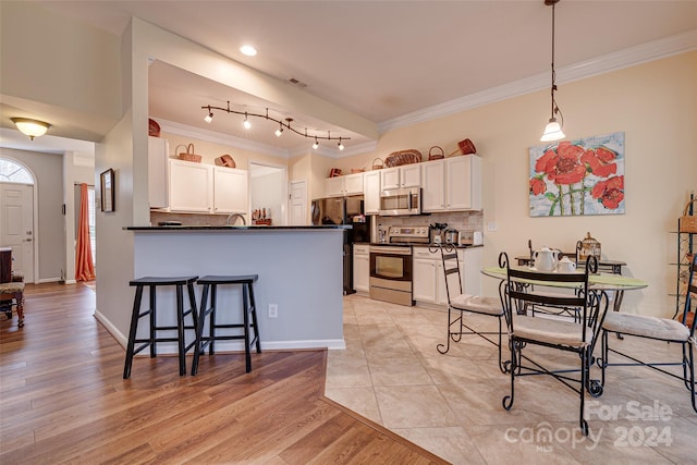 kitchen featuring a breakfast bar, white cabinets, appliances with stainless steel finishes, decorative light fixtures, and kitchen peninsula