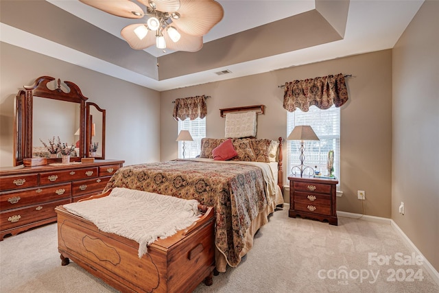 bedroom featuring light colored carpet, a raised ceiling, and ceiling fan