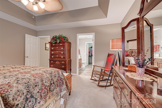 bedroom featuring light carpet, connected bathroom, a tray ceiling, and ceiling fan