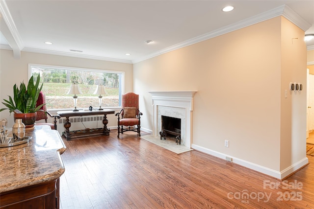 living area with radiator heating unit, a premium fireplace, hardwood / wood-style floors, and ornamental molding