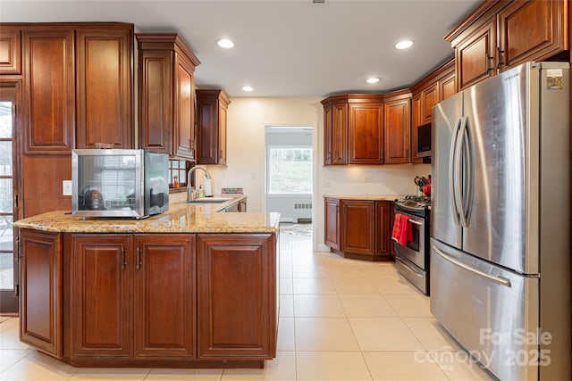 kitchen with light stone countertops, appliances with stainless steel finishes, kitchen peninsula, radiator, and sink