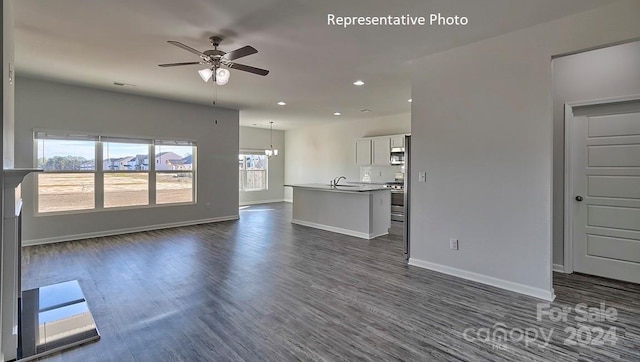 unfurnished living room featuring ceiling fan with notable chandelier, dark hardwood / wood-style flooring, and sink