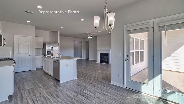 kitchen featuring appliances with stainless steel finishes, a kitchen island with sink, hardwood / wood-style flooring, white cabinetry, and hanging light fixtures