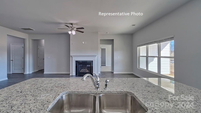 kitchen with dark hardwood / wood-style flooring, ceiling fan, light stone counters, and sink