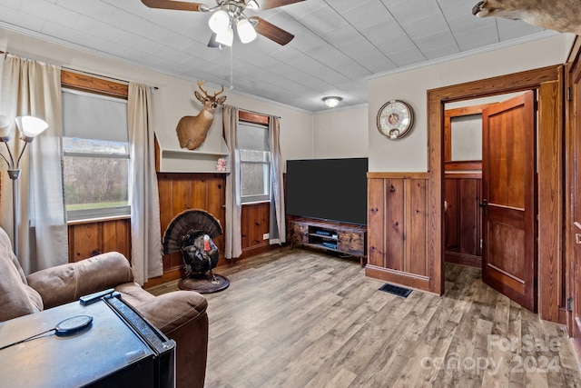 living room with light hardwood / wood-style floors, ceiling fan, ornamental molding, and wood walls