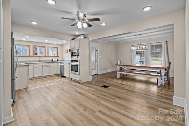 kitchen featuring stainless steel appliances, sink, decorative light fixtures, white cabinets, and light hardwood / wood-style floors