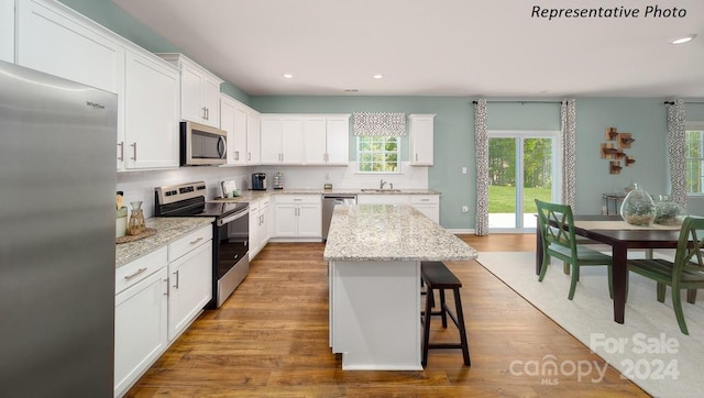 kitchen with appliances with stainless steel finishes, a center island, hardwood / wood-style flooring, and white cabinetry