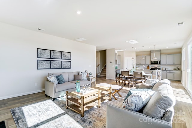 living area with stairway, recessed lighting, baseboards, and light wood-type flooring