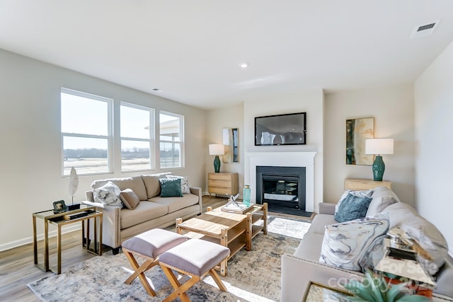 living room with light wood finished floors, visible vents, baseboards, and a glass covered fireplace