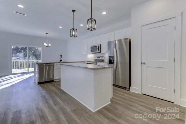 kitchen featuring white cabinets, a center island with sink, hanging light fixtures, light stone countertops, and appliances with stainless steel finishes