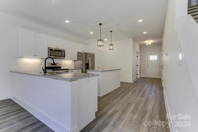 kitchen with white cabinets, hanging light fixtures, light wood-type flooring, light stone countertops, and appliances with stainless steel finishes