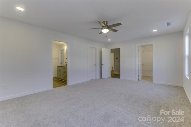 unfurnished bedroom with ceiling fan, ensuite bathroom, light colored carpet, a walk in closet, and a closet