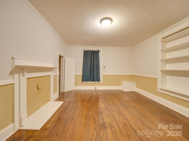 unfurnished living room with a textured ceiling, built in shelves, crown molding, and hardwood / wood-style floors