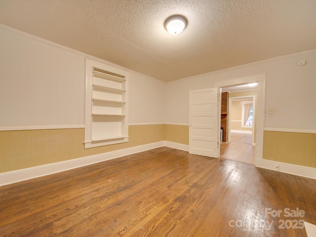 unfurnished room with crown molding, built in features, hardwood / wood-style floors, and a textured ceiling