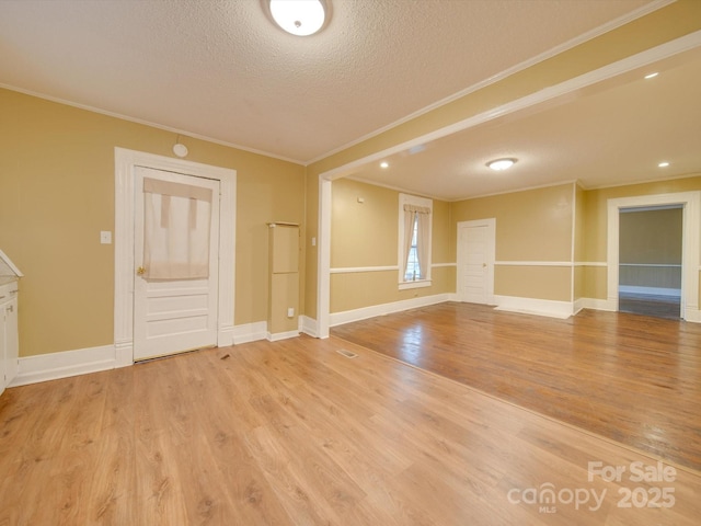 spare room featuring crown molding, a textured ceiling, and light hardwood / wood-style flooring