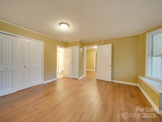 unfurnished bedroom with a closet, ornamental molding, a textured ceiling, and light hardwood / wood-style flooring