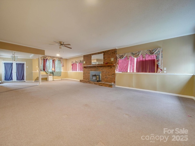 unfurnished living room with carpet flooring, a wood stove, ceiling fan, and ornamental molding