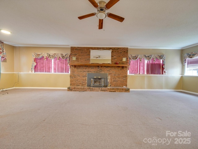 unfurnished living room with carpet flooring, a wood stove, plenty of natural light, and ceiling fan