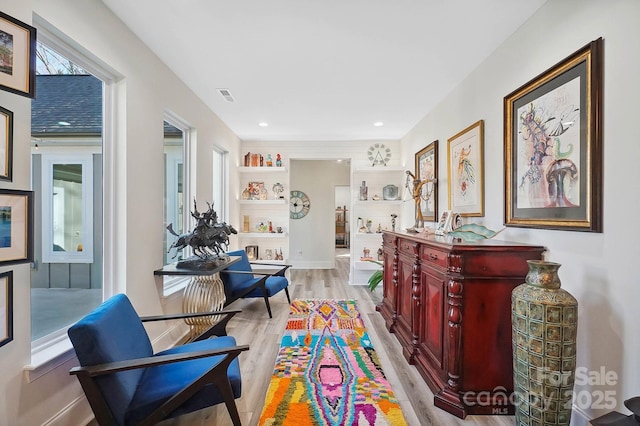 living area with built in shelves, light wood-type flooring, and a wealth of natural light