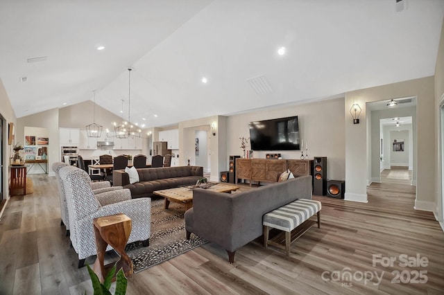 living room with ceiling fan with notable chandelier, light hardwood / wood-style floors, and high vaulted ceiling