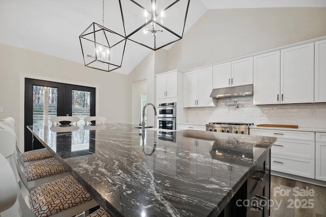 kitchen featuring a large island with sink, white cabinetry, a kitchen breakfast bar, and dark stone countertops