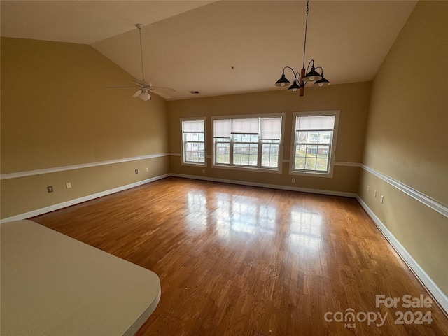 unfurnished dining area featuring wood-type flooring, ceiling fan with notable chandelier, vaulted ceiling, and a wealth of natural light