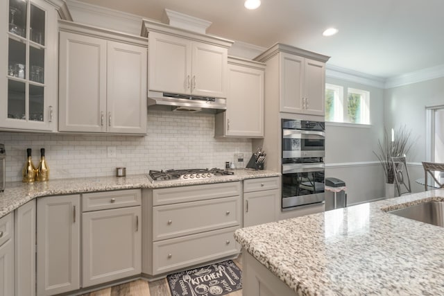 kitchen with appliances with stainless steel finishes, backsplash, light stone counters, and ornamental molding