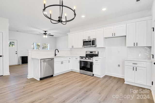 kitchen with white cabinets, appliances with stainless steel finishes, ceiling fan with notable chandelier, and hanging light fixtures