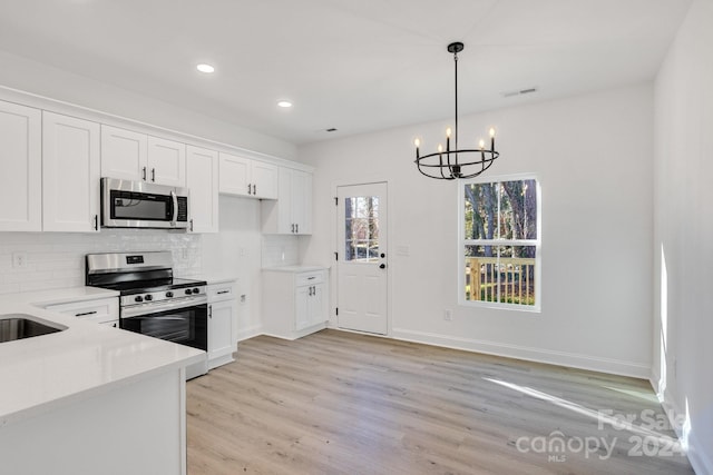 kitchen with white cabinets, backsplash, stainless steel appliances, and light hardwood / wood-style flooring